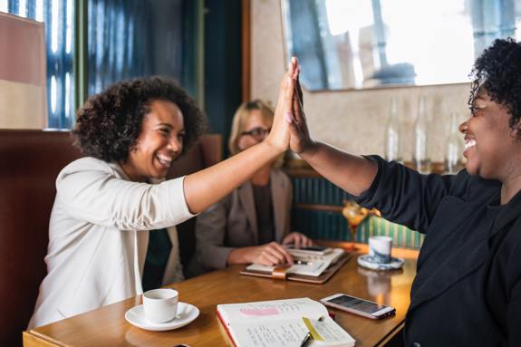 Women high-fiving in restaurant booth. 